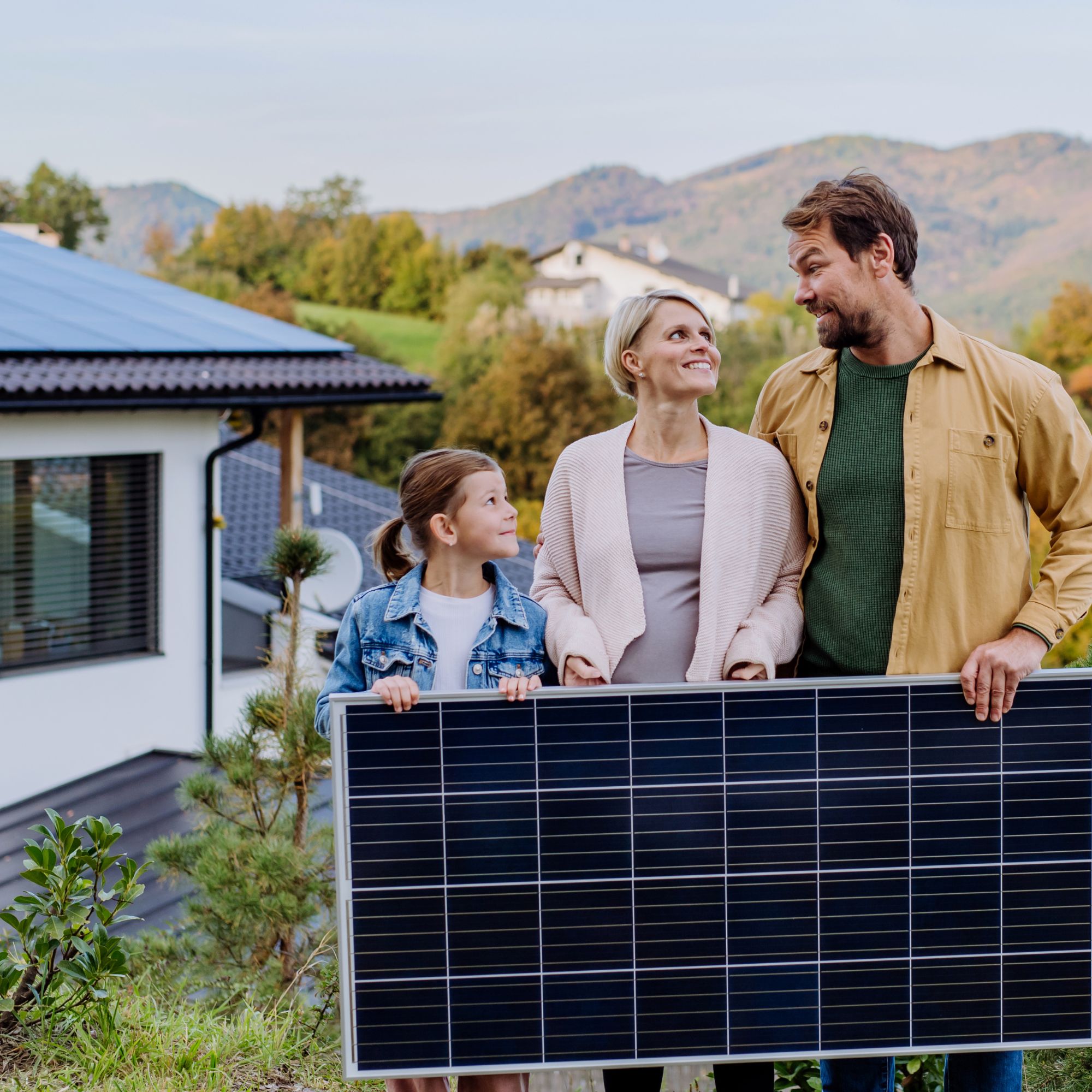 Glückliche Familie vor ihrem Haus, die ein Solarmodul in der Hand hält - Nachhaltige Energielösungen für Zuhause.
